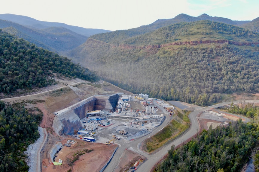 An aerial view of a construction site on the side of a hill, surrounded by bushland.