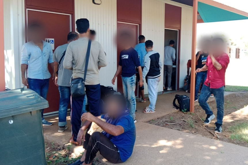 A group of men outside a public toilet with their faces digitally blurred.