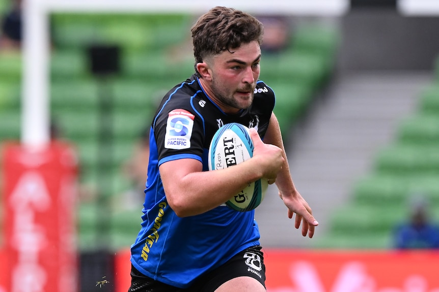 A man playing rugby runs with the ball.