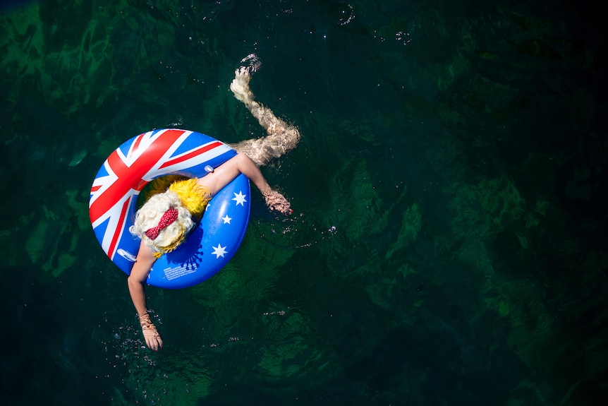 A birdsye perspective of a swimmer with blue floatie and blonde wig swimming in the ocean.