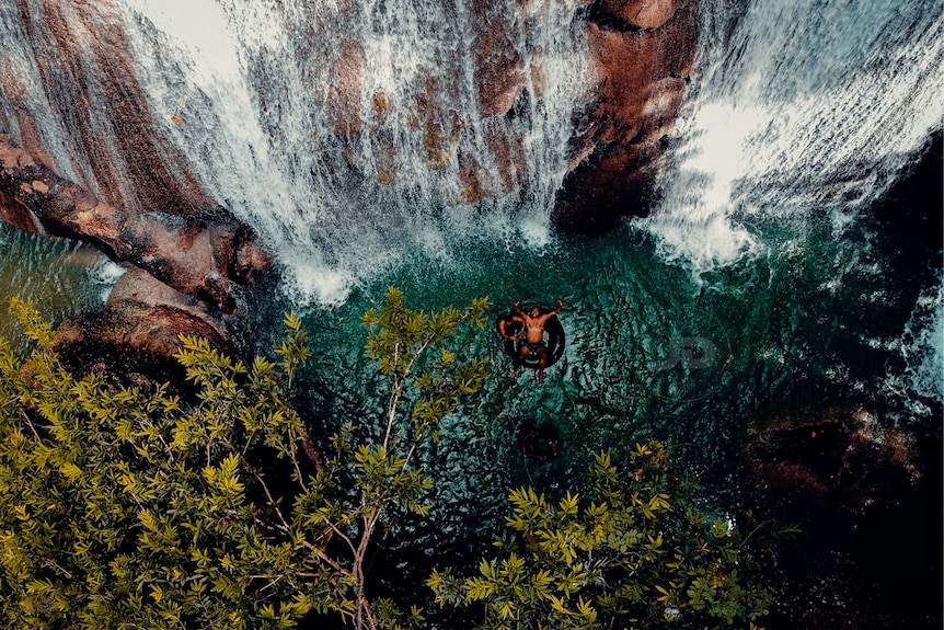 A photo of a man in a rubber tube under a waterfall.