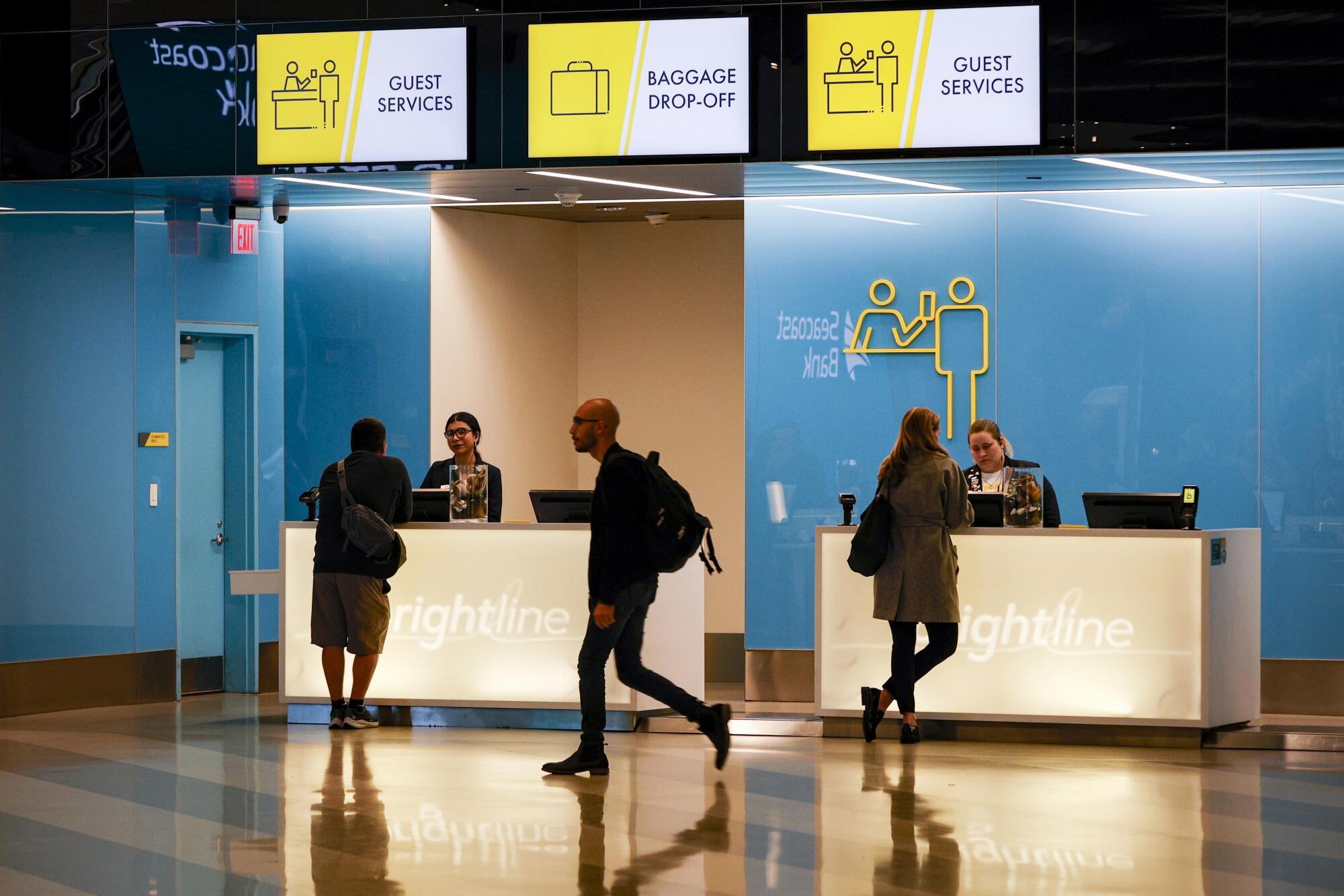 A man walks past people talking to employees behind counters, with signs for baggage and guest services overhead