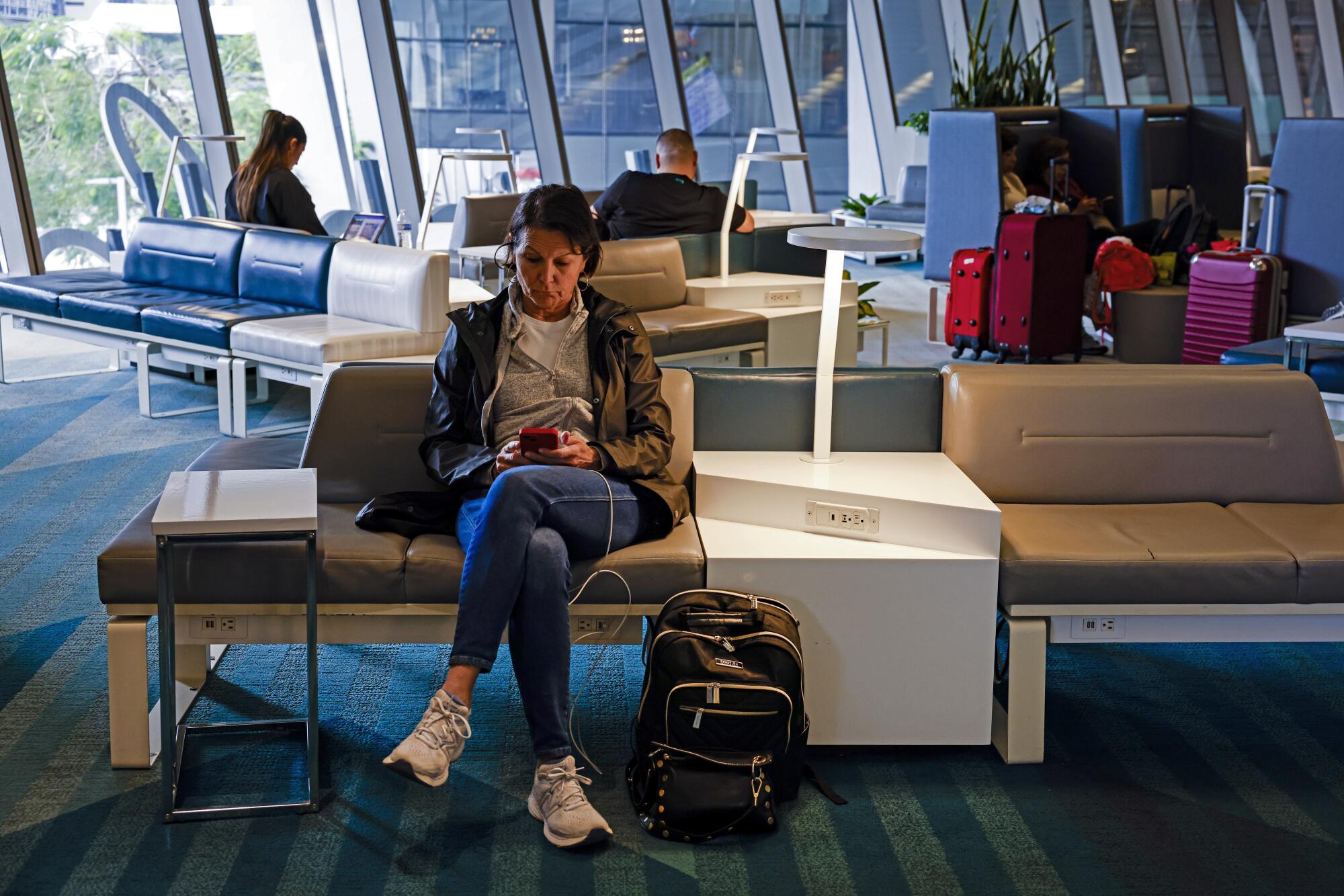 People with luggage wait in a lounge with glass windows 