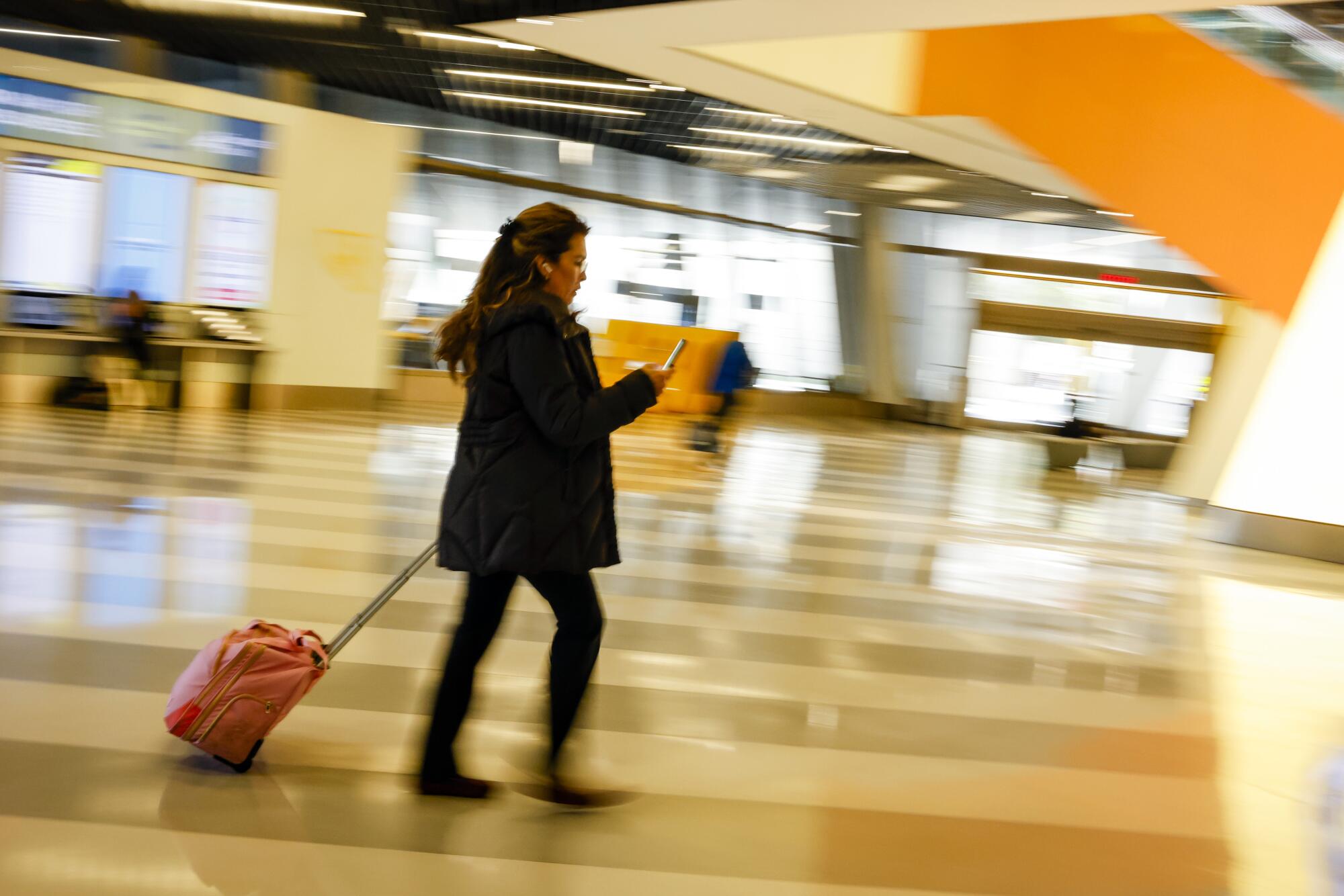 A woman in dark clothes wheels her luggage by the handle while walking