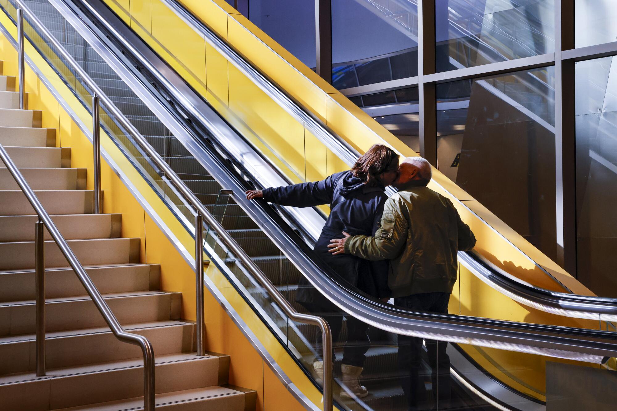 A couple kissing while riding an escalator alongside a set of stairs 