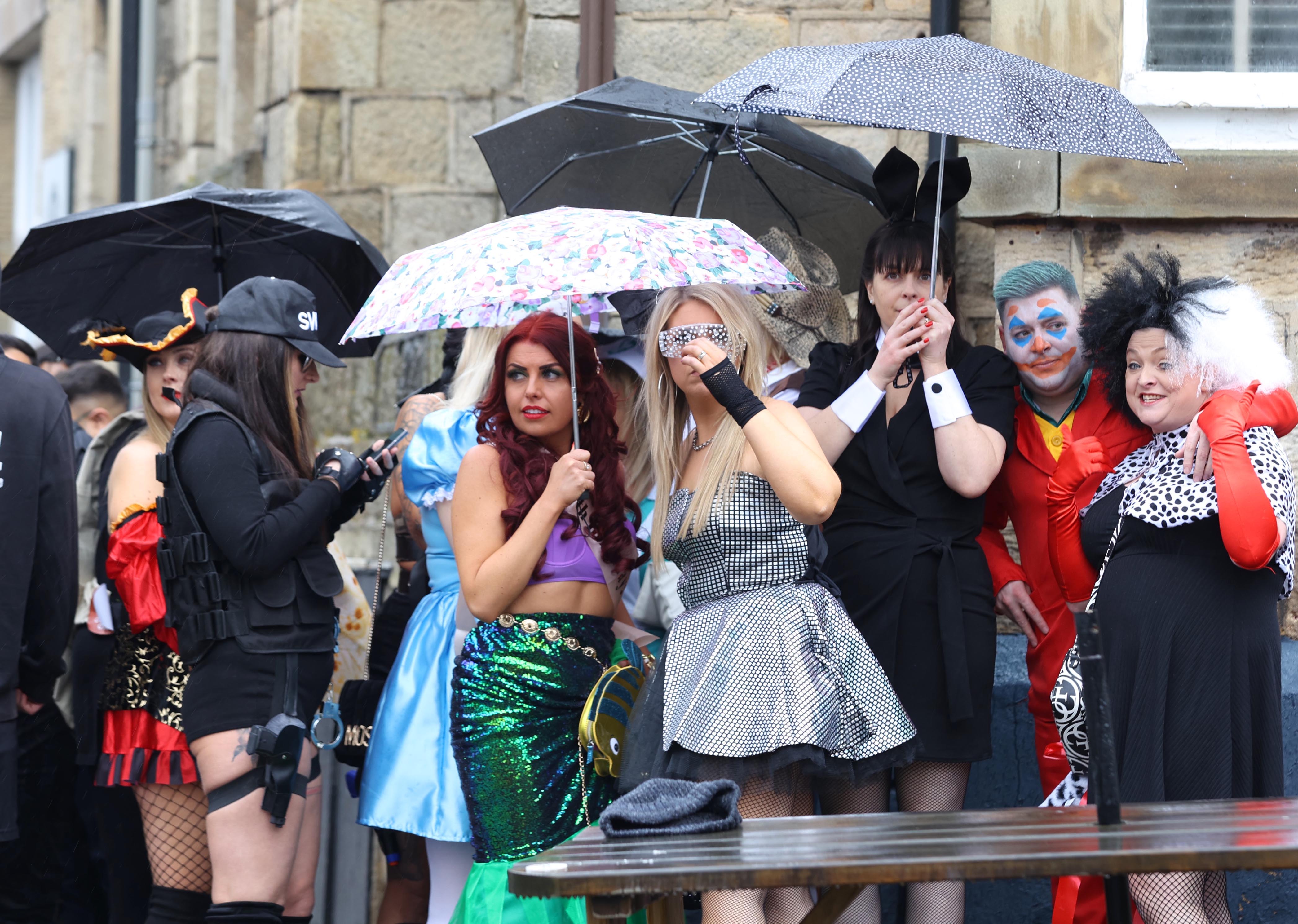 Groups gathered outside in the rain sheltered by umbrellas