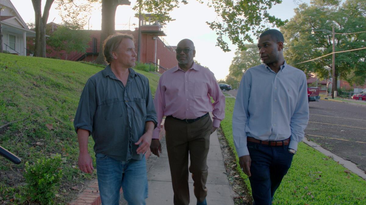 Three men walk down a sidewalk