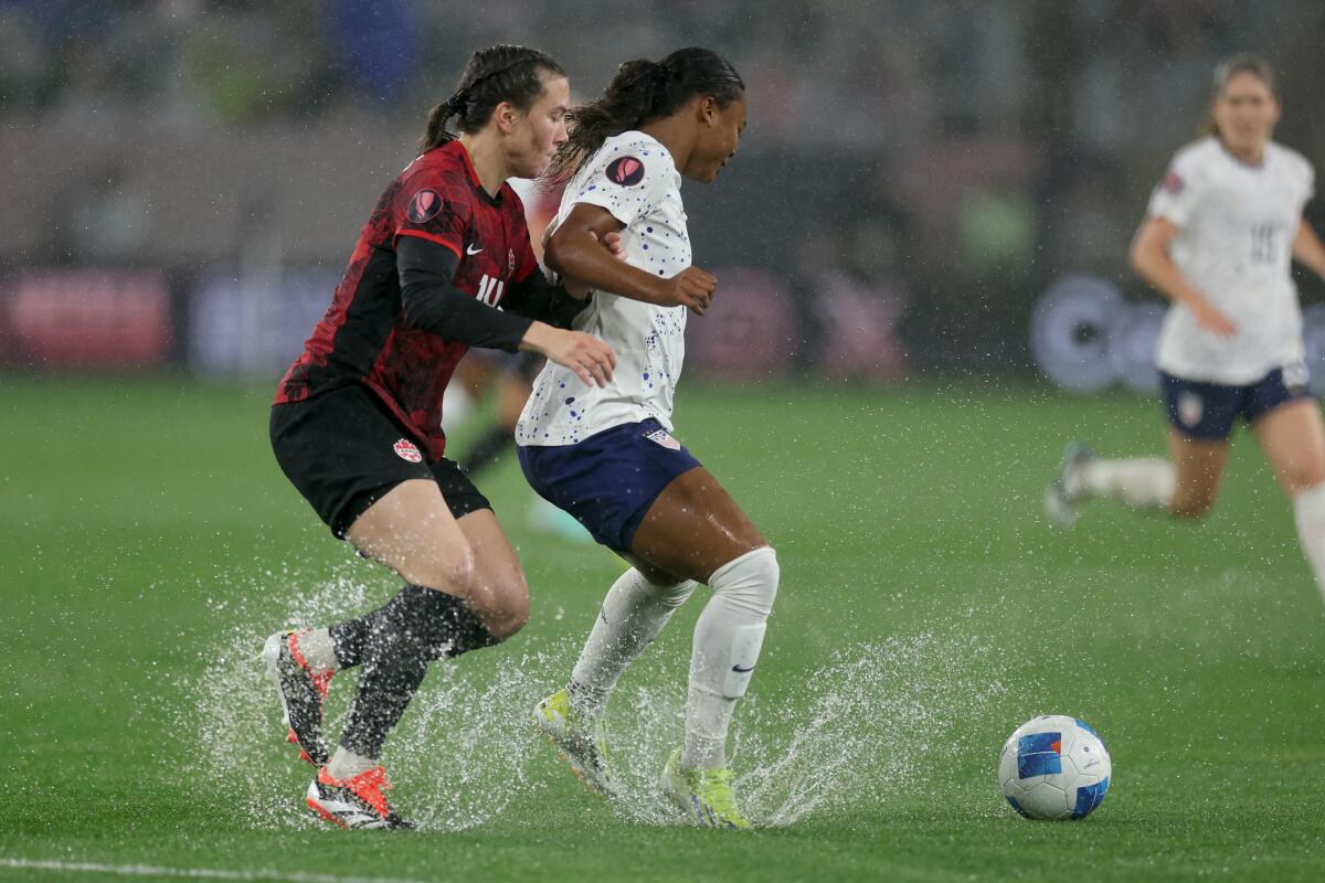 Canada's Vanessa Gilles and American Jaedyn Shaw push through water while chasing the ball during a match 