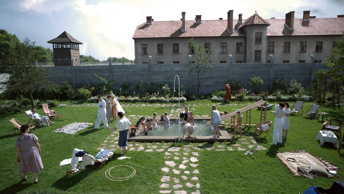 A movie still shows a family relaxing in a swimming pool as a watch tower looms in the distance. 