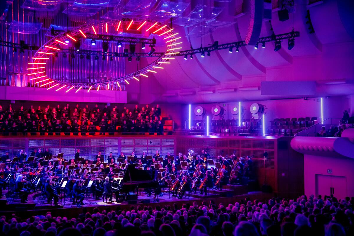 A symphonic orchestra is bathed in pink and purple light while on stage.