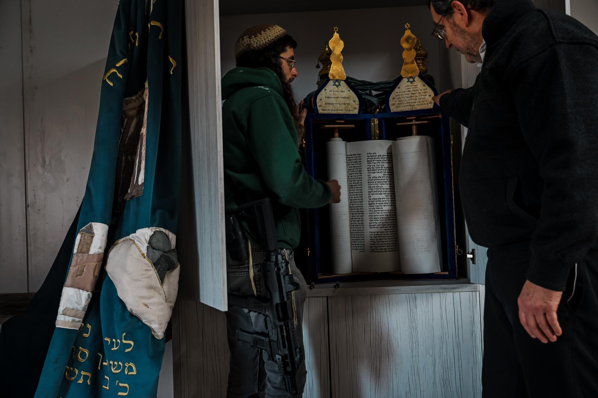 Two men standing, looking at the scrolls of the Torah inside a synagogue.