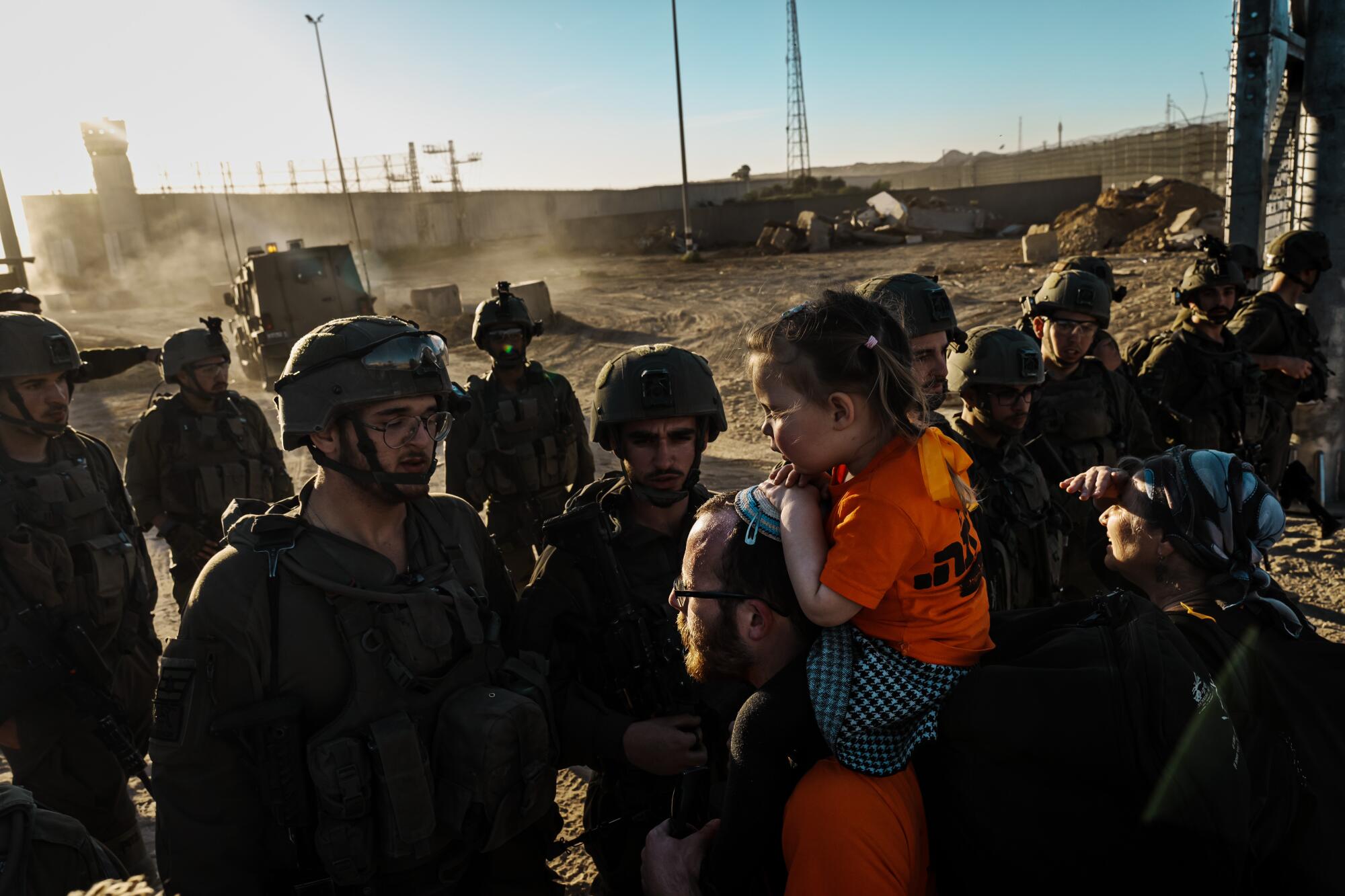 Troops standing in the way of people seeking to pass, including a man with a small child on his shoulders