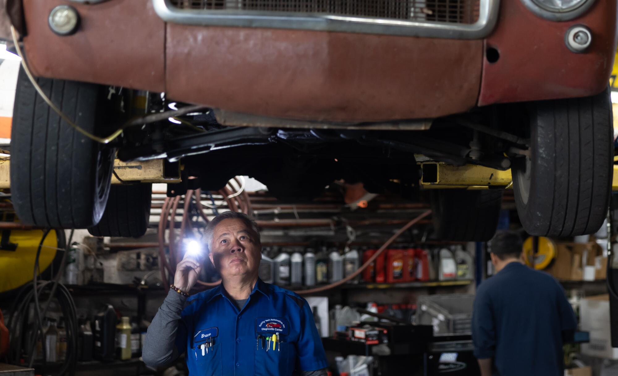 A man underneath a raised vehicle, pointing a flashlight as he looks up at its underbody