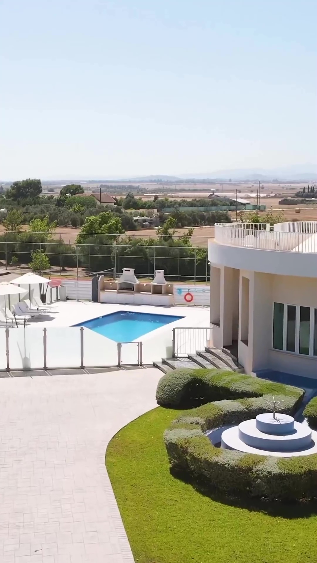 The beautiful white villa is surrounded by grass, stone slab paths and trees