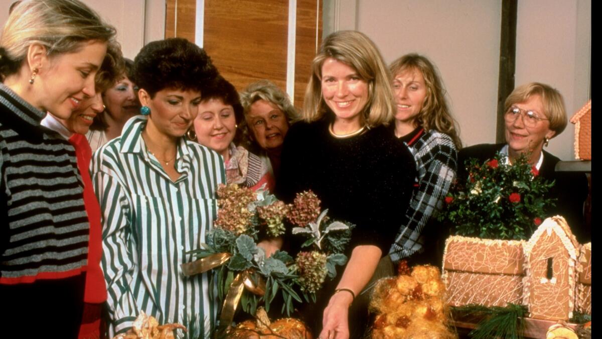 A young woman displays holiday decorations for several women standing around her.