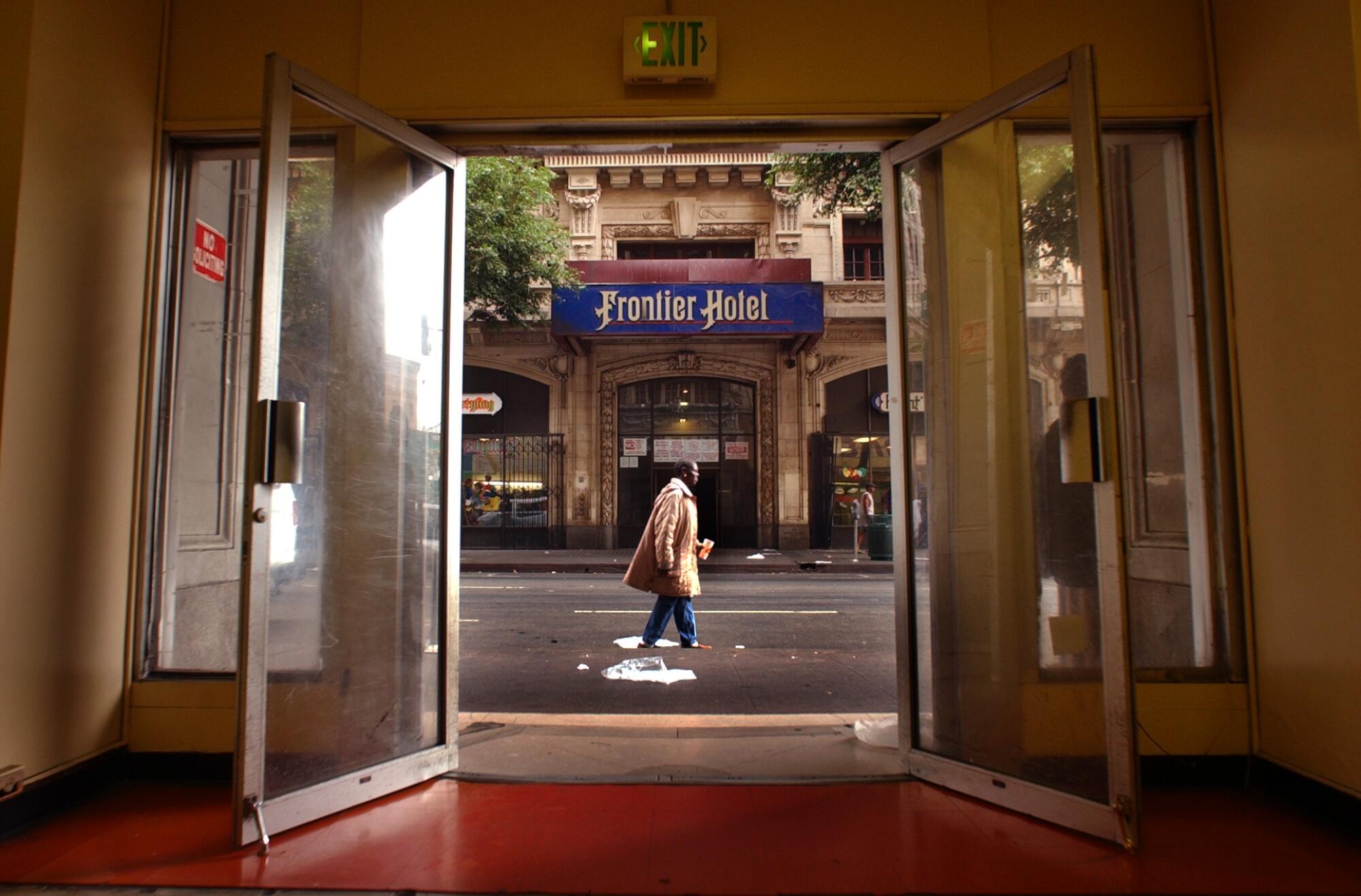 Looking through the lobby doors of the Rosslyn Hotel, a woman can be seen as she makes her way along 5th Street.