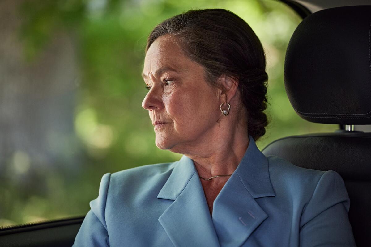 A woman in a blue suit looks out a window.