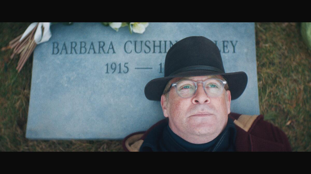 A man reclines on a gravestone, looking up at the sky.