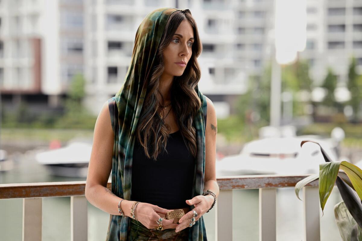 A woman stands pensively on a balcony overlooking the water.