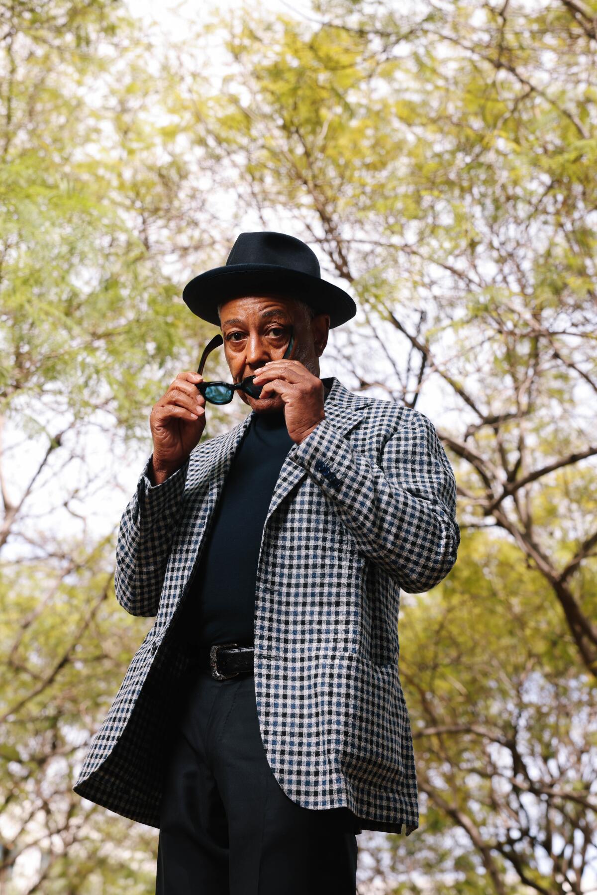 A man in a suit and hat poses with sunglasses