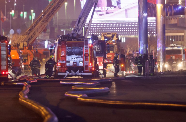 Fire engines outside the venue. Cranes have been deployed. Fire hoses are on the ground. Firefighters are working near the truck and at the scene. 