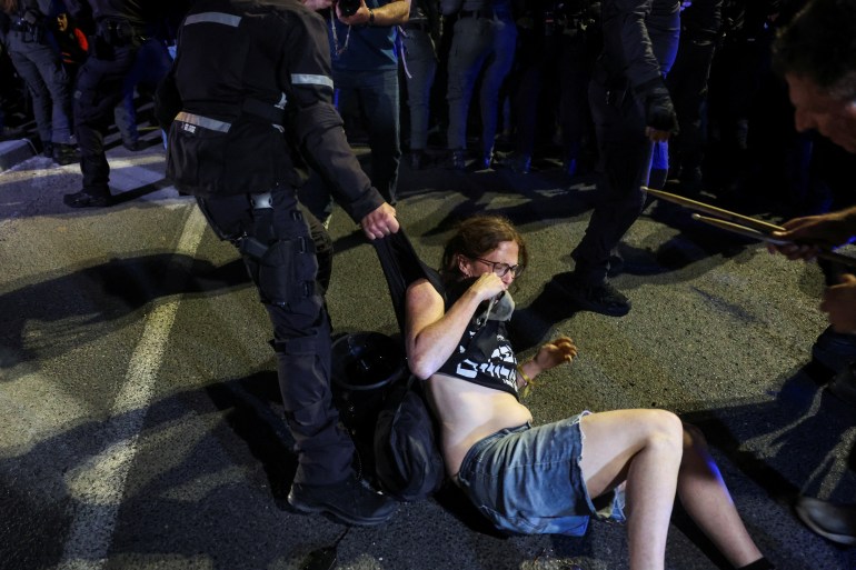 An officer holds a demonstrator's clothing as anti-government protesters launch a prolonged demonstration 