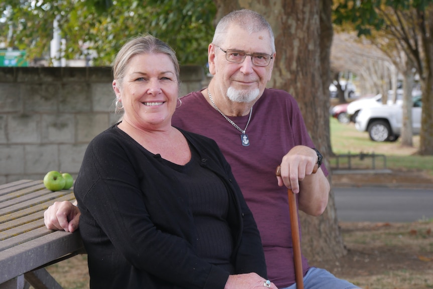 A woman and a man sitting together. The man is holding a walking stick. 