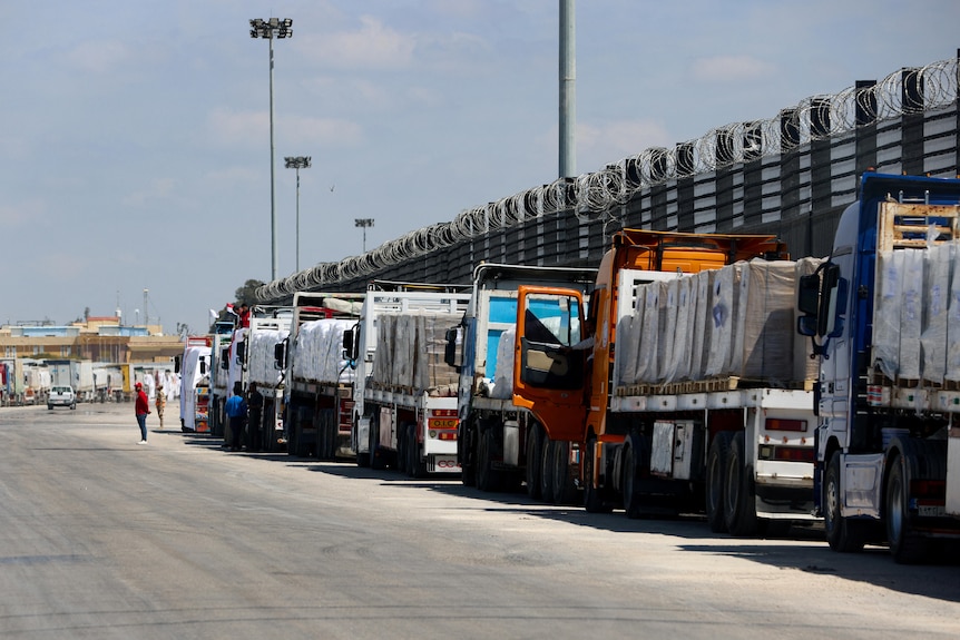 A line of trucks on the side of a road next to a fence.