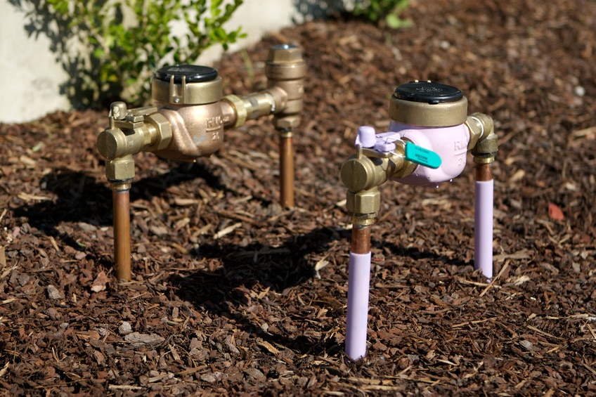 Two water metres side by side in a garden bed