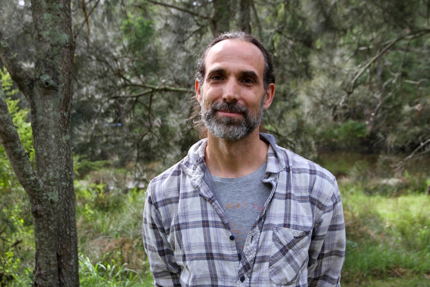 Man with long grey black hair and facial hair, wearing checkered shirt in national park