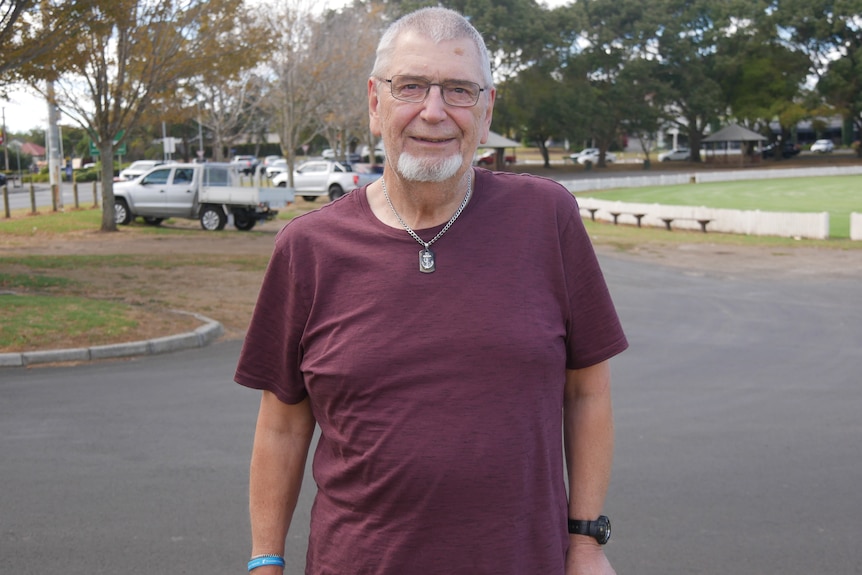 A man wearing a red shirt smiling at the camera, using a walking stick. 