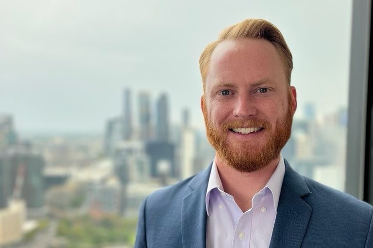 Man with red hair and beard smiles wearing navy blue suit