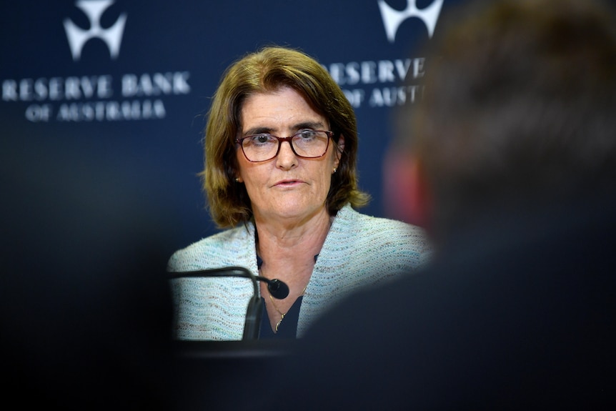 Michele Bullock, looking at journalists, wearing a light blazer, standing at a podium, during a press conference