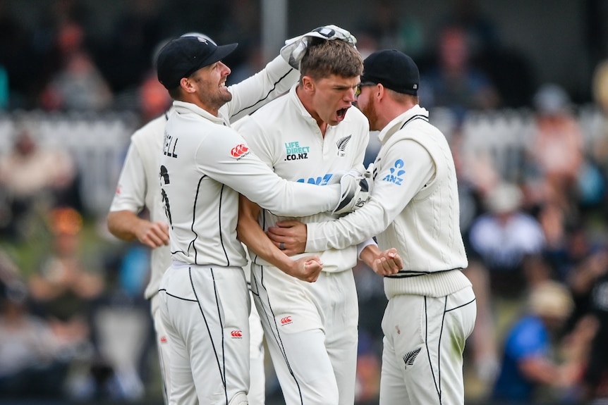 Ben Sears clenches both fists and yells in delight as teammates hug him