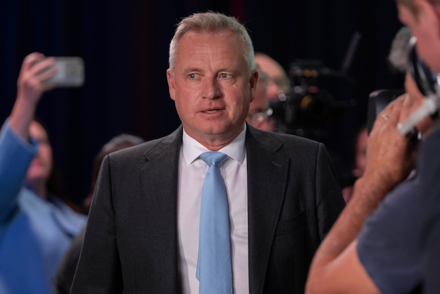 Jeremy Rockliff walks through a crowded room and cameras film him.