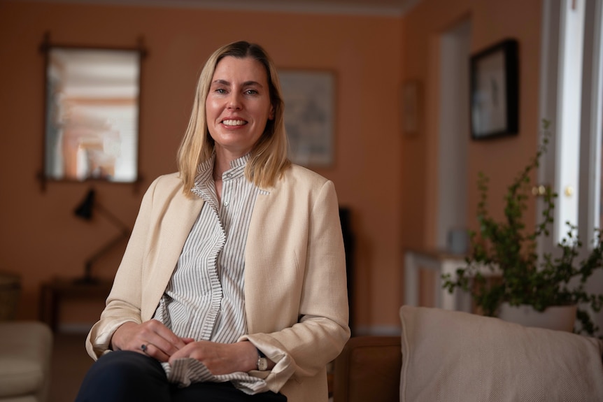 A lady in a living room, sitting down and smiling at the camera.