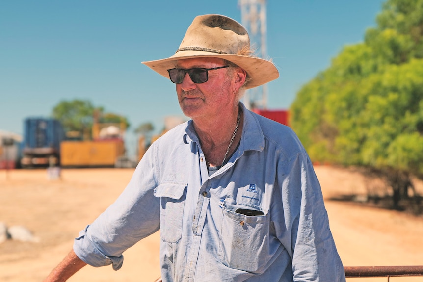 a man stands with an oil and gas rig behind him 