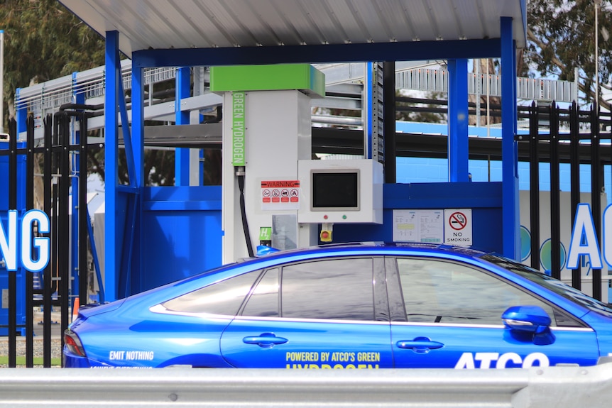 A blue car sits at a blue fuel pump.