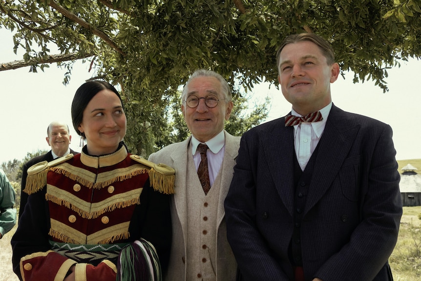 Leonardo DiCaprio, Lily Gladstone and Robert De Niro stand side-by-side in characters of Killers of the Moon film