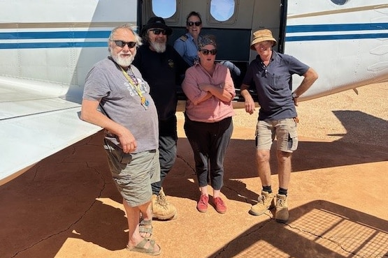 five people standing around a small plane 