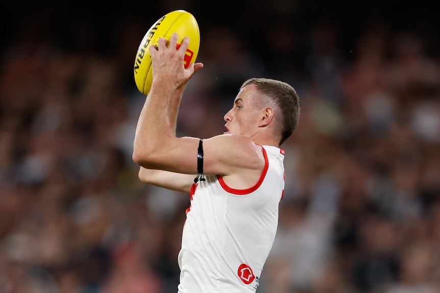 A Sydney Swans AFL player rises to take a clean mark as a Collingwood defender stands watching.