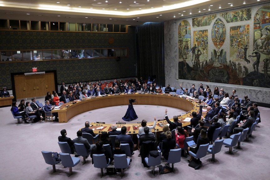 People sit behind a round table in a large room facing each other ready to vote