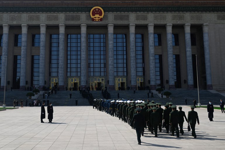 people wearing dark coloured uniforms line up in straight lines outside a building with grey columns