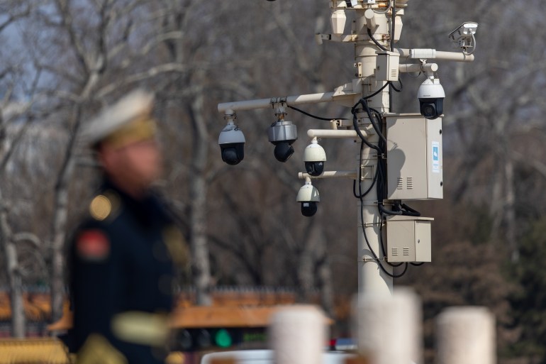 a soldier in the foreground is blurry while surveillance cameras can be seen behind him