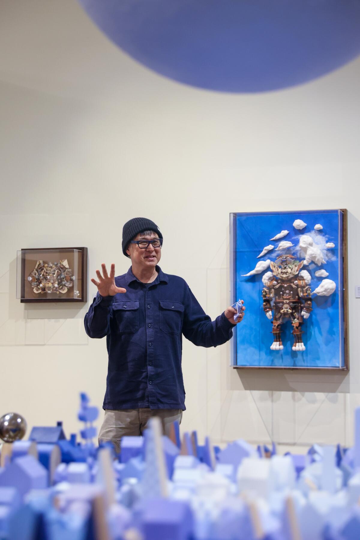 A man gestures in front of a painting at a museum.