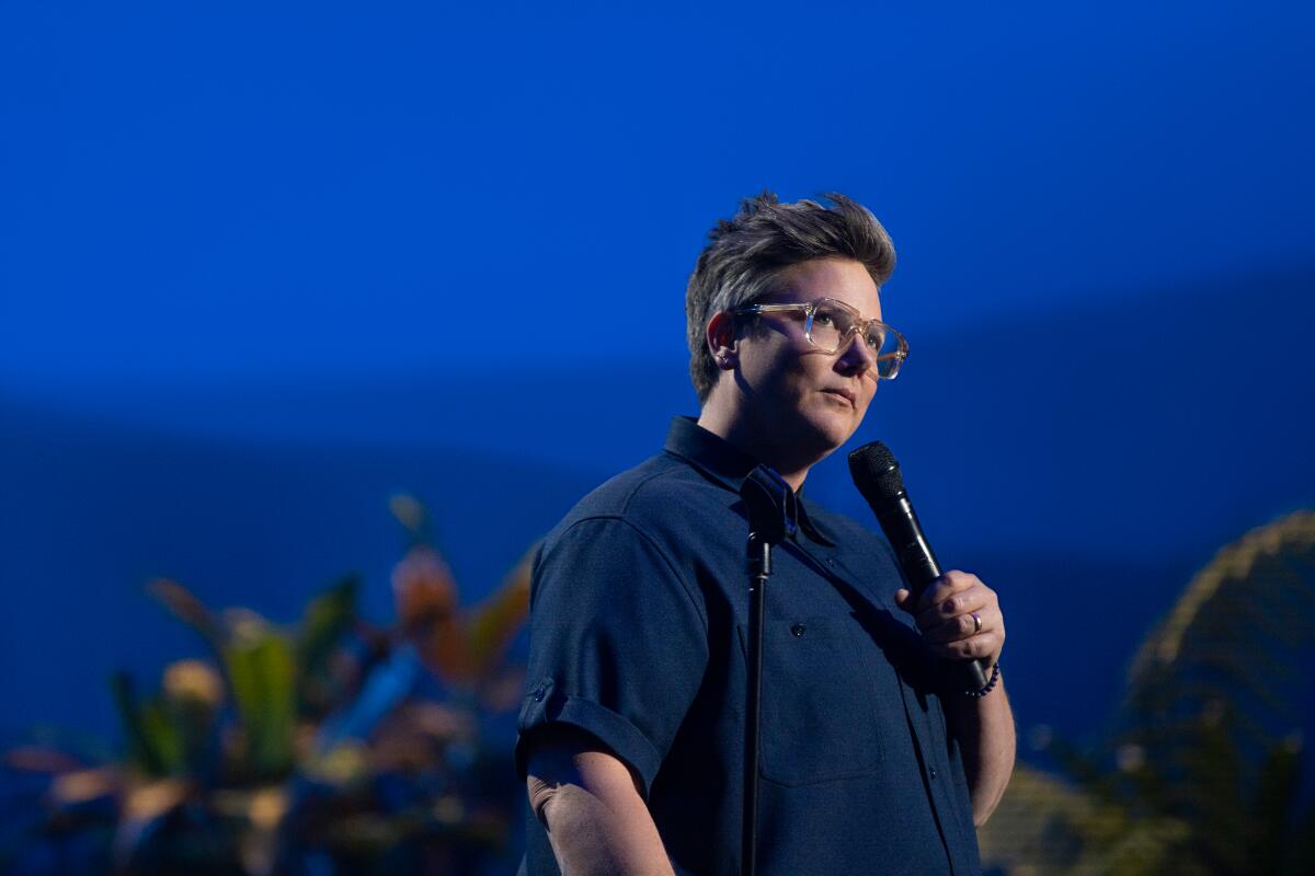 A woman holds a microphone onstage, with a background of ocean images.