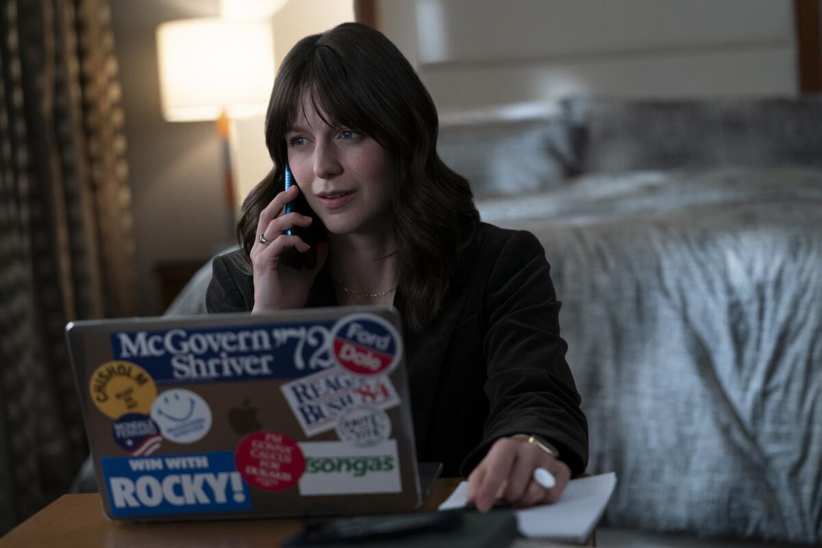 A woman with a cellphone to her ear and a laptop computer in front of her.