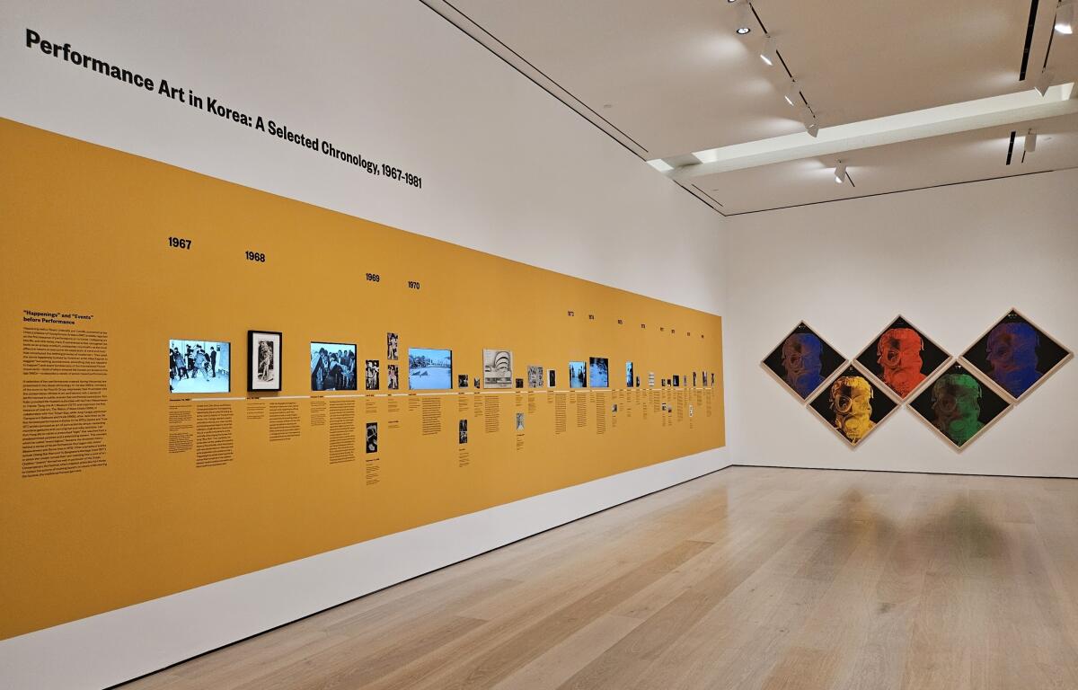 A timeline of still and video images is  displayed on a yellow museum wall. Five silkscreen images are beside it.