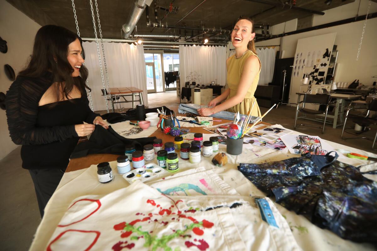 Two women laugh over a sewing table.