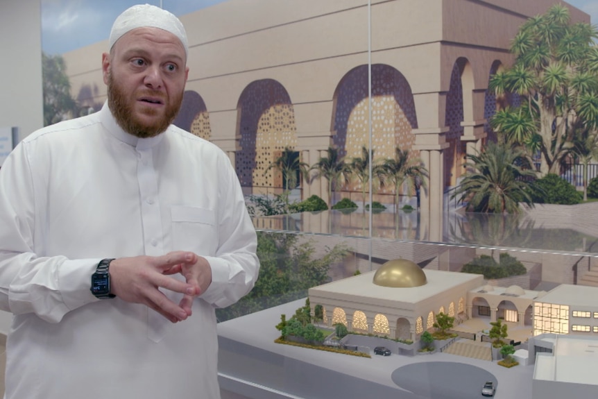 Man in white religious stands in front of model of building